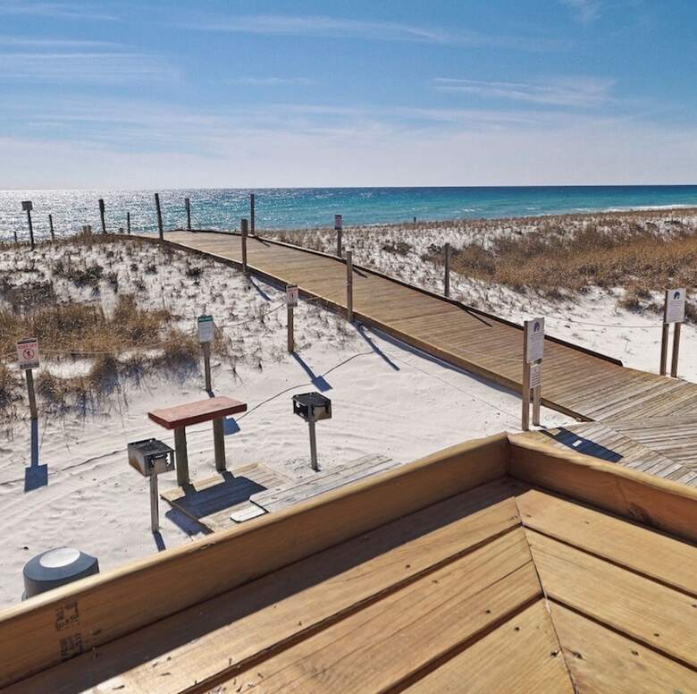 Boardwalk through white sand dunes with barbecue grills leading to the private beach
