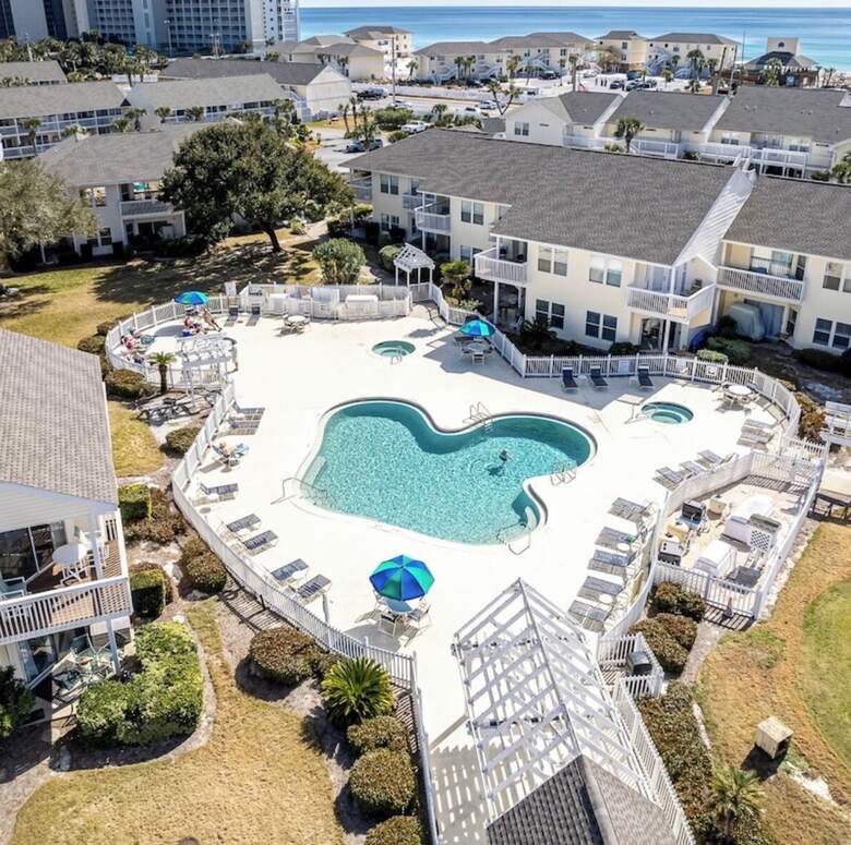 Aerial view of a Sandpiper Cove pool and hot tubs surrounded by condos with the Gulf beyond